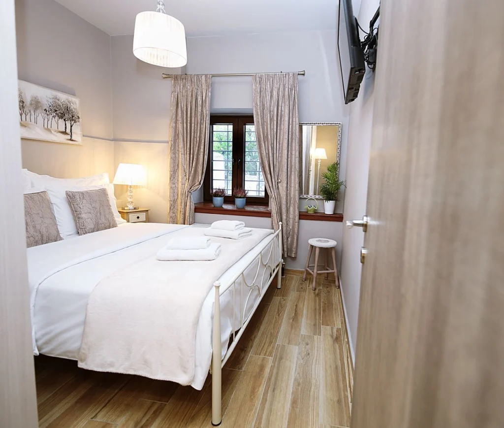 Φωτεινό υπνοδωμάτιο με διπλό κρεβάτι, τηλεόραση και παράθυρο με κουρτίνες.