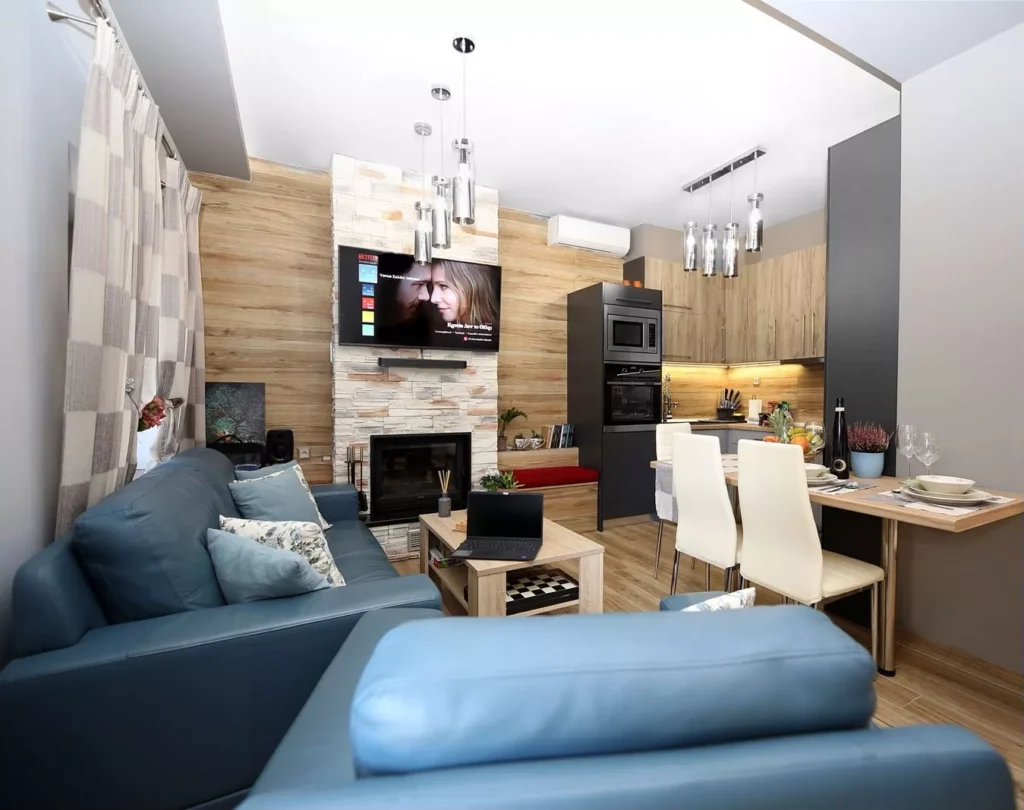 Εσωτερικός χώρος σαλονιού και κουζίνας με μοντέρνα διακόσμηση, τζάκι, τηλεόραση με ταινία Fast & Furious, και τραπέζι φαγητού σερβιρισμένο.