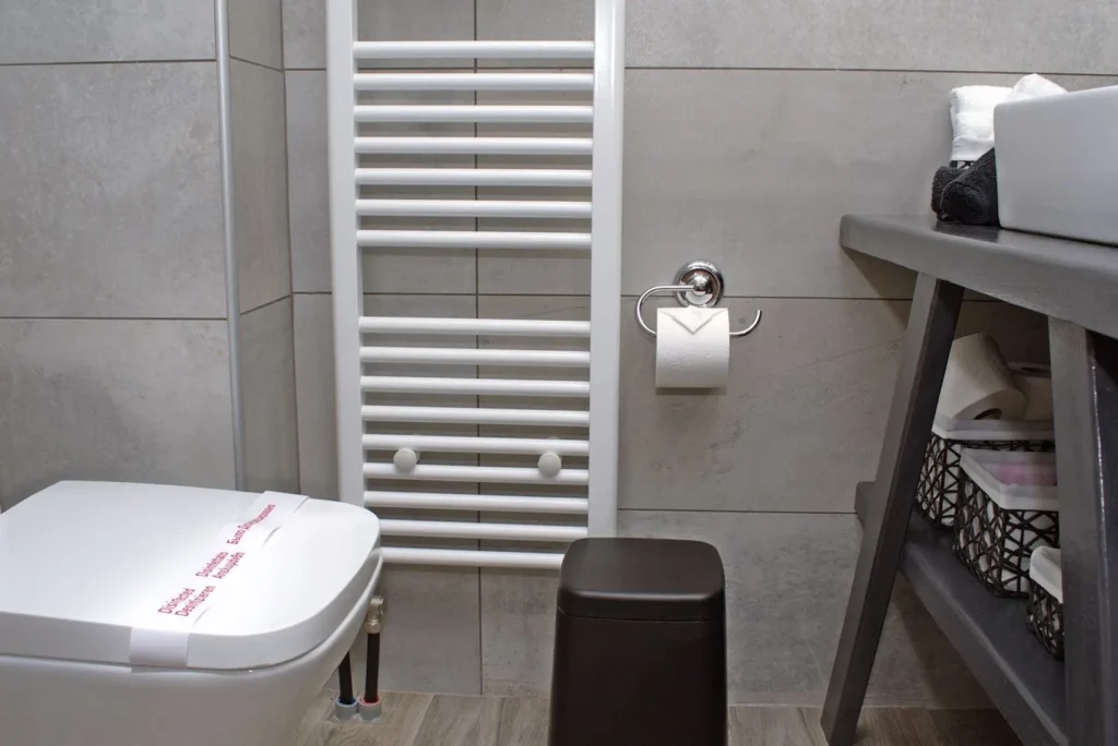 Τουαλέτα επισκεπτών στο Venus Guesthouse με θερμαντικό σώμα, κάδο, ράφι με πετσέτες και καθαρό design